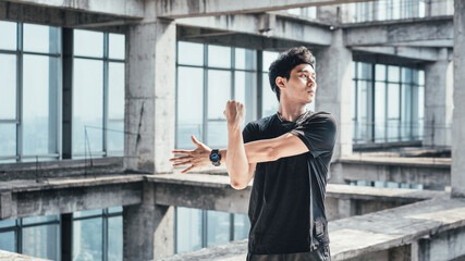 Young Asian man is doing body stretching in an abandoned reinforced concrete building
