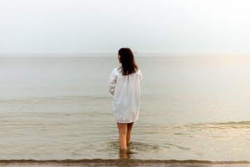 woman walking along beach and sea sunset background.Loneliness and sadness concept.Empty place for text.Back view.
