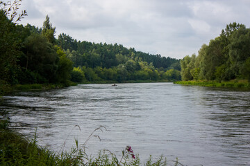 Outskirts of Grodno, Belarus. The Neman River on a cloudy summer day, in the distance on the water - a rubber boat with a man sitting in it.