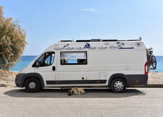 Motorhome is parked near sea beach. The owners left, leaving the dog to guard the van.
