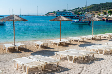 Summer vacation destination. Straw sunshades and sunbeds on the empty  beach with sea in the background.
