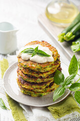 Stack of zucchini fritters served with squacquerone cheese and basil leaves. White wooden background.