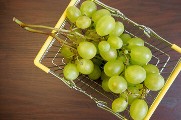 in a mini-basket from the supermarket there is a white grape variety on a brown background. top...