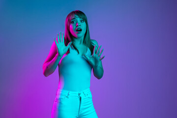 Portrait of young scared girl isolated on blue studio background in neon pink light filter. Concept of human emotions, facial expression, youth, sales, ad.