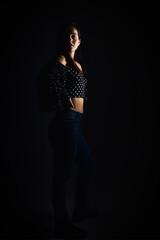 Naklejka premium Full length portrait of a young girl with a serious look looking towards the camera, on a dark studio background