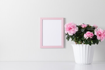 Pink frame mockup on white wall with pink flowers in pot decoration. Front view