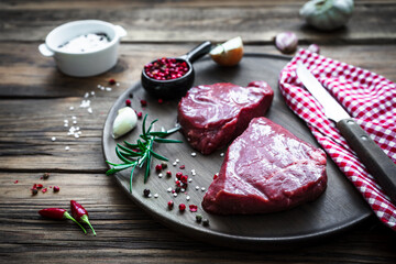 Nahaufnahme von zwei rohen Rindfleisch Steaks und Gewürz Zutaten auf einem runden Holz...