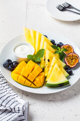 Fresh fruit charcuterie dessert grazing platter on white plate, light tiles background. Vegan food concept.