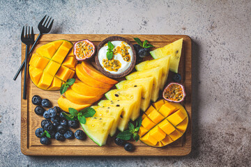 Tropical fruit charcuterie platter on wooden board, dark background.