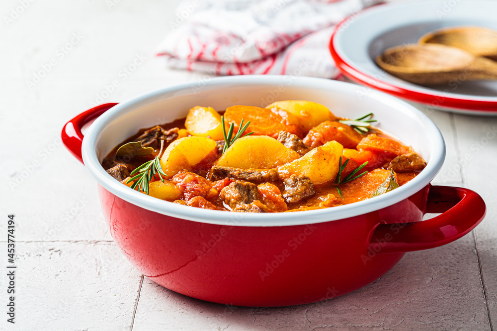 Canvas Prints Beef stew with potatoes and carrots in tomato sauce in red pot, gray  background.