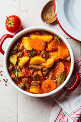 Beef stew with potatoes and carrots in tomato sauce in red pot, gray  background.