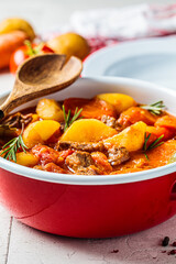 Beef stew with potatoes and carrots in tomato sauce in red pot, gray  background.