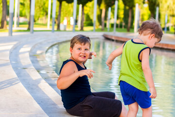 Children in the park dip their feet in the fountain they are very happy. Have fun and rejoice on a summer day at the fountain.