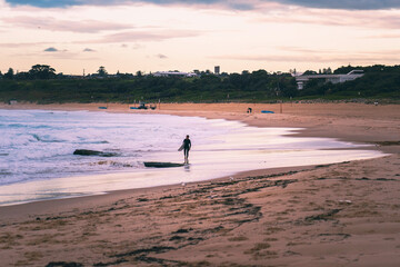 Fototapeta na wymiar silhouette surfer at sunset walking along the sand at the beach