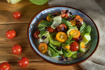 Vegetarian salad of pac choi cabbage, kiwi, tomatoes, kumquat, microgreen sprouts on a wooden background. Side view, close up, hard light.
