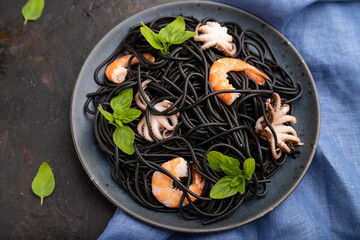 Black cuttlefish ink pasta with shrimps or prawns and small octopuses on gray wooden background. Top view, selective focus.