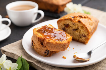 Homemade cake with raisins, almonds, soft caramel and a cup of coffee on a black concrete background. Side view, selective focus.