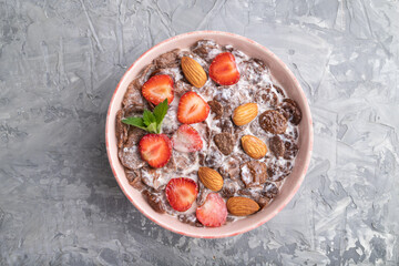 Chocolate cornflakes with milk, strawberry and almonds in ceramic bowl on gray concrete background. Top view.