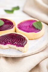 Sweet tartlets with jelly and milk cream with cup of coffee on a white wooden background. Side view, selective focus.