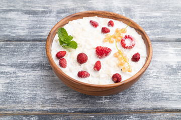 Rice flakes porridge with milk and strawberry in wooden bowl on gray wooden background. Side view, copy space.