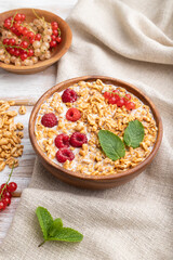 Wheat flakes porridge with milk, raspberry and currant in wooden bowl on white wooden background. Side view, close up.