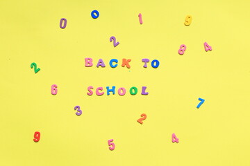 Words from multi colored letters on a yellow background. Expression Back to school on paper background. Layout of letters on a yellow background. Many multicolored letters and numbers