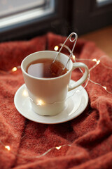 drinks and objects concept - cup with mesh tea infuser ball and garland lights on window sill at home