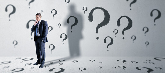 Thoughtful young european business man standing in concete interior with question mark sketch....