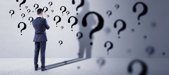 Thinking young european businessman standing in concete interior with question mark sketch....