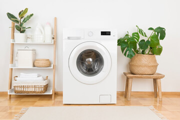 Modern washing machine and plants in rustic laundry room interior