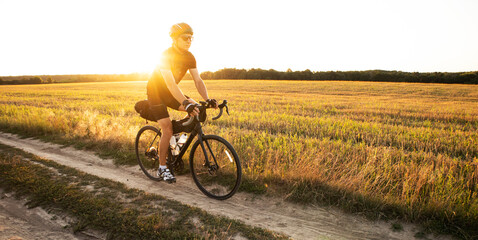 Obraz premium Bike traveler riding through the field at sunset on bicycle with bags