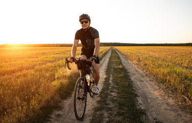 Fototapeta premium Bike traveler riding through the field at sunset on bicycle with bags