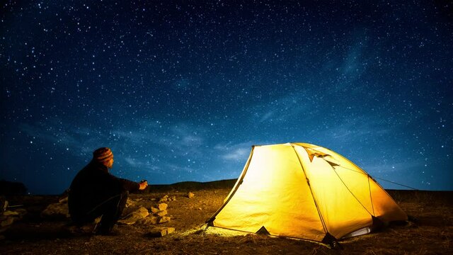Traveler near the glowing camping tent on the background of the twinkling starry sky. Cinemagraph.
