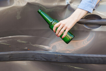 Unknown female hand holding bottle with beer white sitting behind wheel of broken car, road...