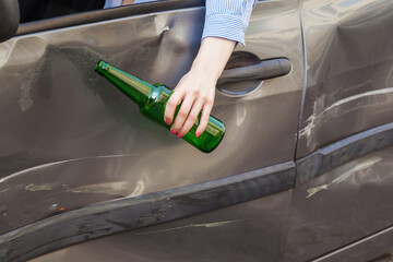 Faceless portrait of female hand hanging from the car window with bottle of alcohol beverage,...