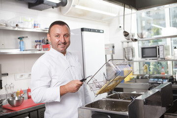 Professional chef smiling to the camera, making french fries at restaurant kitchen, copy space
