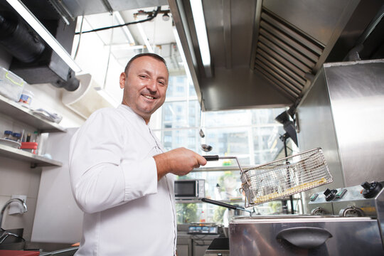 Low angle shot of a cheerful male chef smiling to the camera, while making french fries
