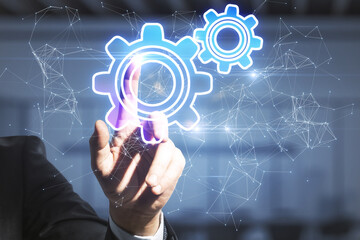 Close up of businessman hand pointing at abstract glowing gear wheels on blurry background with connections. Digital engineering and industry concept.