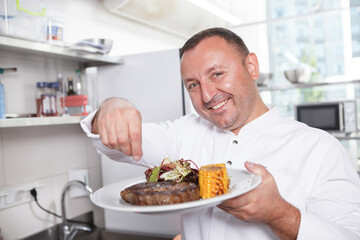 Close up of a happy male chef smiling salting beef steak on a plate