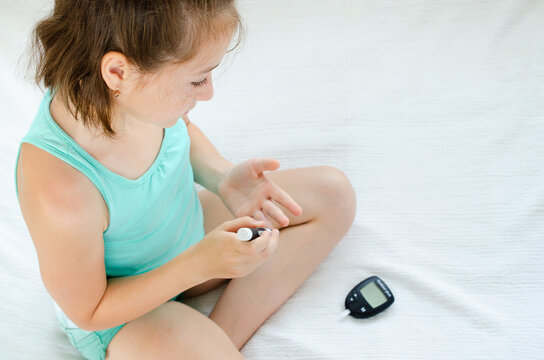 Little girl checking blood sugar level using lancelet and glucometer at home.