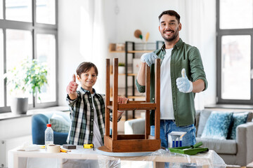 furniture renovation, diy and home improvement concept - happy smiling father showing thumbs up to his son sanding old round wooden table with sponge
