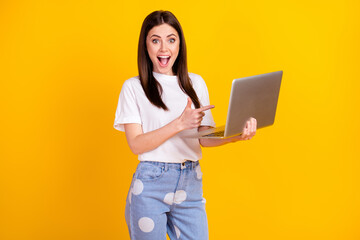 Photo of young girl happy positive smile point finger laptop advice choice suggest isolated over yellow color background