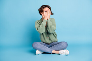 Photo of cute scared young lady dressed green cardigan sitting legs folded arms cover face isolated blue color background