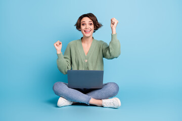 Full length photo of lucky funny lady wear cardigan sitting floor typing modern device rising fists isolated blue color background