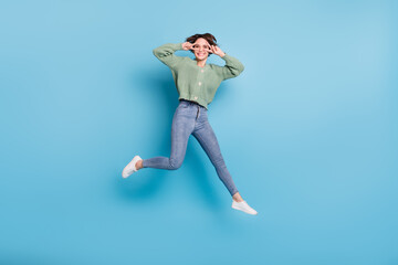 Fototapeta na wymiar Full length photo of adorable sweet young girl dressed green cardigan jumping high v-signs cover eyes isolated blue color background