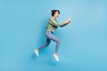 Fototapeta na wymiar Full length photo of purposeful excited young lady wear green cardigan jumping typing modern device isolated blue color background