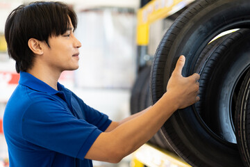 Asian male worker checking new tire wheel on shelves shelf at wheel store. Salesman examining new tire at workshop. Car service and Maintenance concept