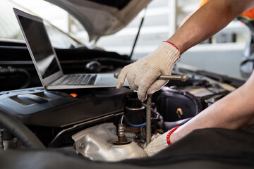 Hands of male mechanic worker maintaining car engine under hood of car at the repair garage. Male car mechanic working using wrench tool for examining, repair and maintenance at car service shop