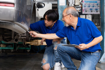 Asian technician worker maintenance car engine underneath lifted car. Group of mechanic vehicle...