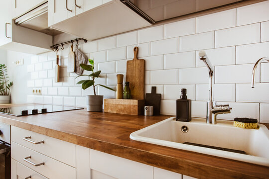 Kitchen brass utensils, chef accessories. Hanging kitchen with white tiles wall and wood tabletop.Green plant on kitchen background